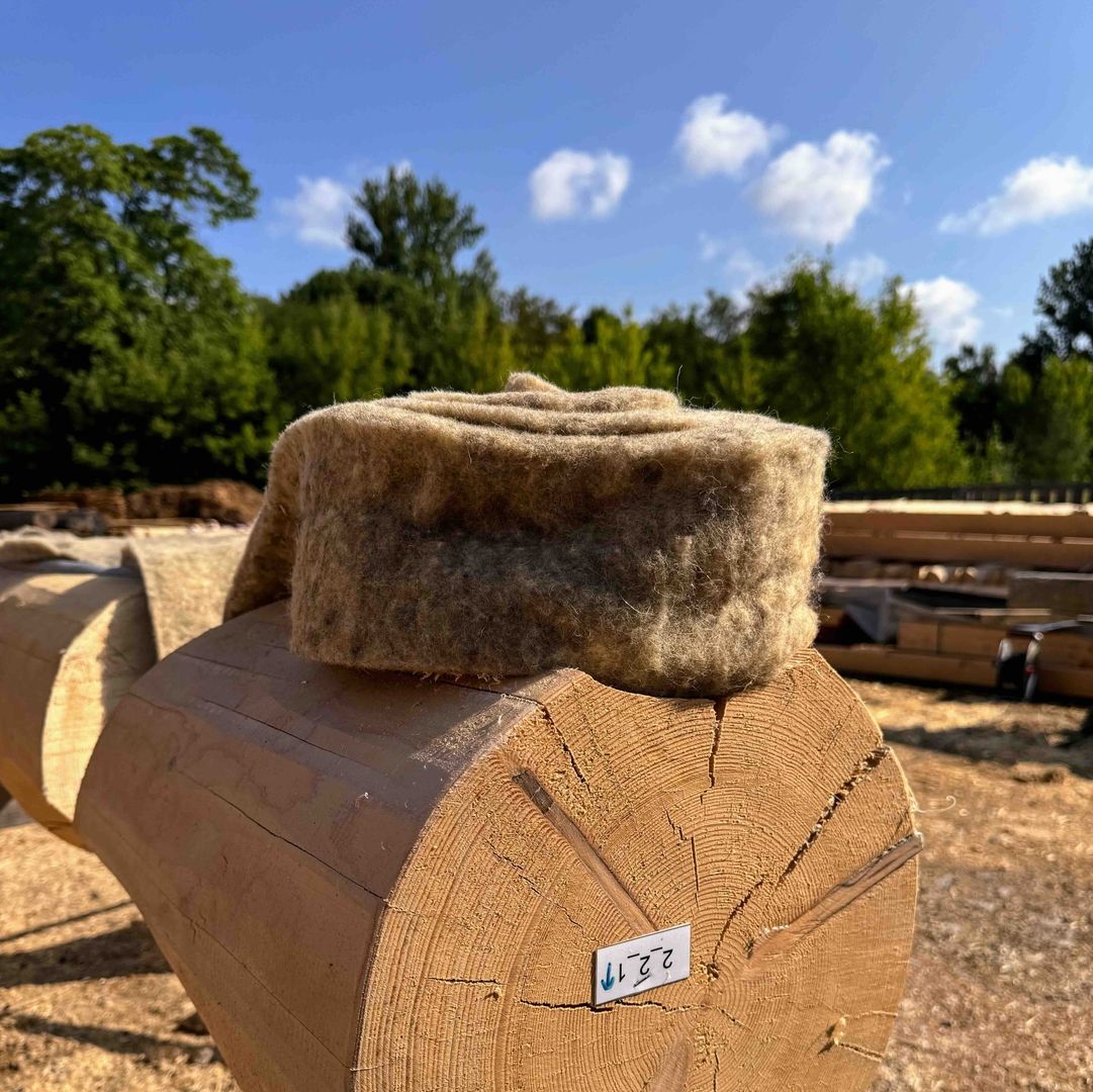 Rolle aus ökologischer Schafwolle liegt bereit zur Montage auf einem Blockhausstamm.